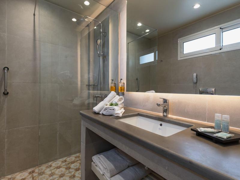 Modernes Badezimmer mit grauen Fliesen, großem Spiegel, Waschbecken und Handtüchern auf Ablage.