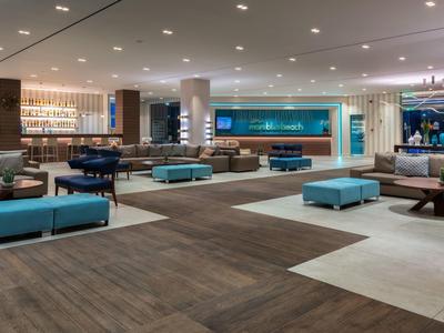 Großer, moderner Lobbybereich mit blauen Sitzbänken, Teppichboden und warmem Licht.