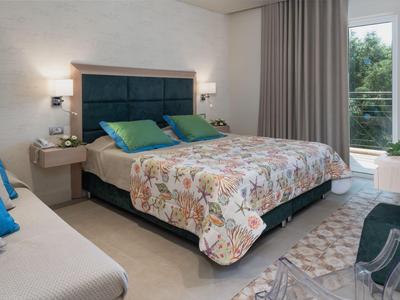 Chambre confortable avec grand lit, coussins colorés et lumière du jour vive.