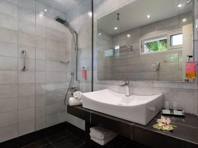 Großer blauer Pool mit Liegestühlen, grünem Rasen und Bäumen vor Bergen bei klarem Himmel.