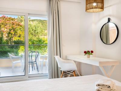 Modernes Schlafzimmer mit weißem Bett, Tisch, Stuhl, rundem Spiegel und Balkon mit Stühlen.