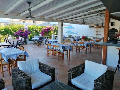 Überdachter Außenbereich eines Restaurants mit Tischen und weißen Stühlen, blumenreiche Begrünung im Hintergrund.