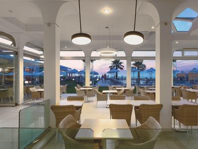 Interno moderno e luminoso di un ristorante con vista sul tramonto e palme.