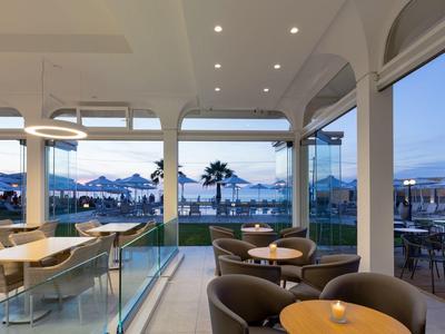 Area lounge moderna dell'hotel con vista sulla piscina all'aperto e palme al tramonto.