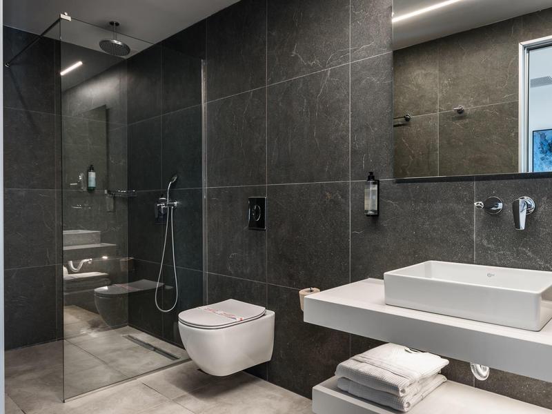 Bagno moderno con piastrelle scure, doccia walk-in e lavabo su mensola sospesa