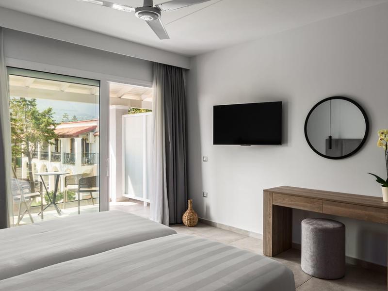 Camera con letto matrimoniale, TV a parete, specchio e balcone con vista sul giardino.