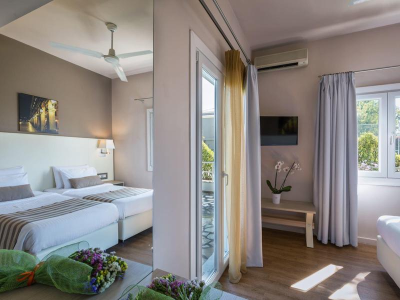 Camera d'hotel moderna con letto matrimoniale, interni luminosi e balcone con vista sul verde.