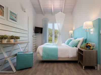 Heller Hotelzimmer mit Doppelbett, türkisfarbenem Kopfteil und weißen Wänden mit Fenster.