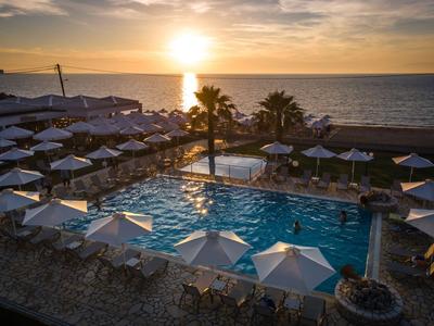 Sonnenuntergang über einem Außenpool mit weißen Sonnenschirmen am Meer.