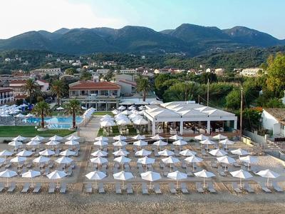 Strand mit weißen Sonnenschirmen und Liegestühlen vor einer Hotelanlage in Berglandschaft.