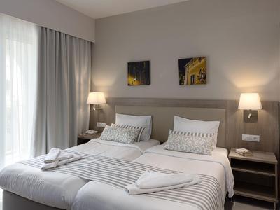 Modernes Hotelzimmer mit zwei Einzelbetten, Nachttischen, Lampen und großem Fenster mit Vorhängen.