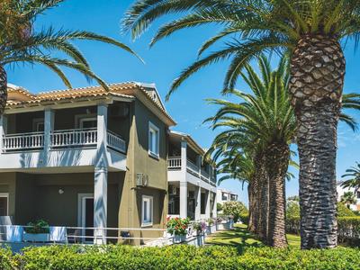 Modern hotelgebouw met balkons omgeven door palmbomen onder een heldere blauwe lucht.