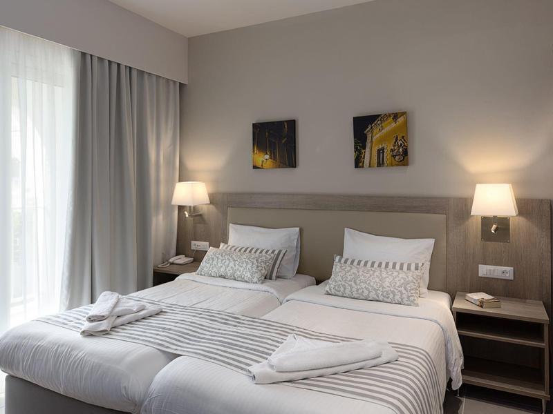 Modernes Hotelzimmer mit zwei Einzelbetten, Nachttischen, Lampen und großem Fenster mit Vorhängen.