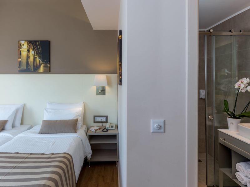 Modernes Hotelzimmer mit Doppelbett, beiger Dekoration und angrenzendem Bad mit Glasdusche.