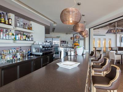 Moderner Hotelbarbereich mit hoher Theke, Barhockern und gut bestückten Regalen.