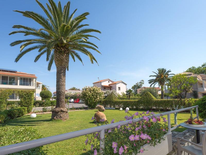 Hotelgarten mit Palmen, Blumen und Sitzbereich bei sonnigem Wetter.