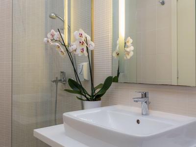 Modernes Bad mit weißem Waschbecken, Spiegel und Orchideen in Vase.