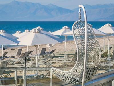 Fauteuil suspendu en osier blanc moderne sur une terrasse avec vue sur la plage et la mer.