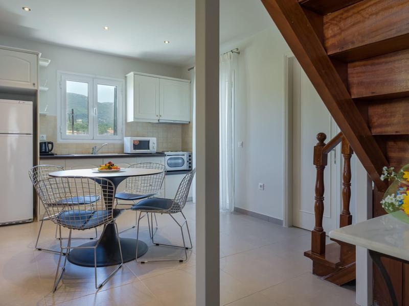 Helle Küche mit Essbereich, weißen Schränken, blauem runden Tisch und Treppe aus Holz.