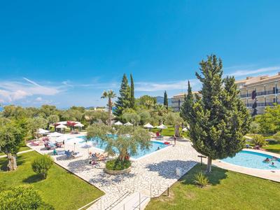 Hotelpool mit Sonnenschirmen, Liegestühlen und grüner Gartenlandschaft unter blauem Himmel.