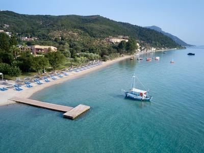 Strand mit Liegestühlen, Steg und Boot in klarem Wasser vor bewaldeten Hügeln.
