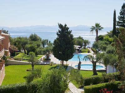 Blick auf einen Pool mit umgebendem Garten und Meer im Hintergrund bei klarem Himmel.