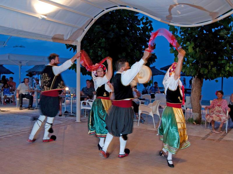 Vier Personen tanzen in traditioneller Kleidung unter einem überdachten Bereich im Freien.