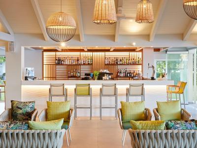 Nowoczesny bar hotelowy z hokerami, lampami koszykowymi i wygodnymi miejscami do siedzenia w jasnych kolorach.