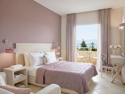 Jasny pokój hotelowy z podwójnym łóżkiem, balkonem i widokiem na morze w świetle dziennym.