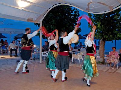Cuatro bailarines con trajes tradicionales bailan bajo un techo de carpa iluminado festivamente.