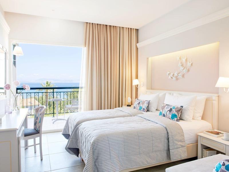 Helles Hotelzimmer mit Doppelbett und Balkon mit Meerblick.