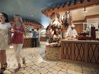 Hotel lobby with guests walking and a chef preparing food in a cozy, rustic area.