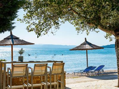 Strand met parasols, ligstoelen en een tafel met stoelen onder bomen.