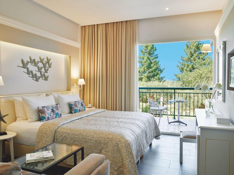 Modernes Hotelzimmer mit großem Bett, Balkon und Blick auf grüne Bäume.