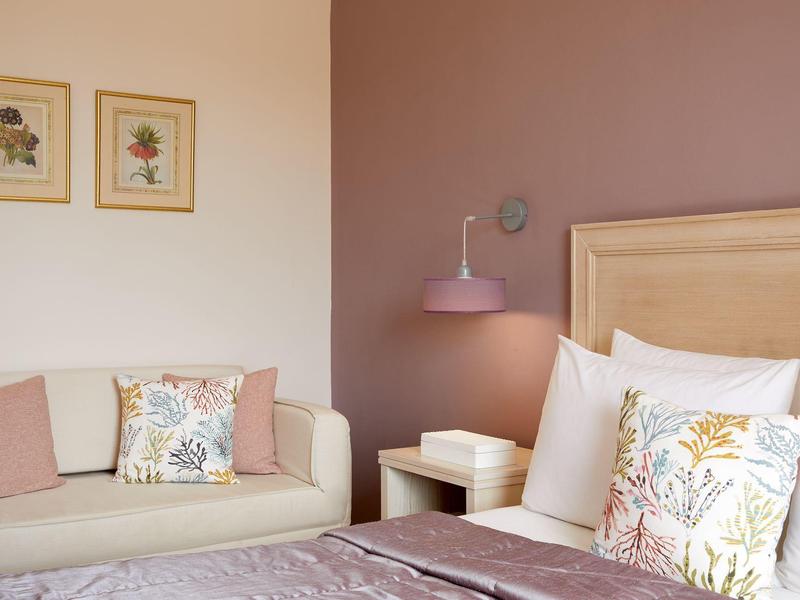 Helles Hotelzimmer mit beiger Couch, farblich abgestimmten Kissen und Pastellwand.