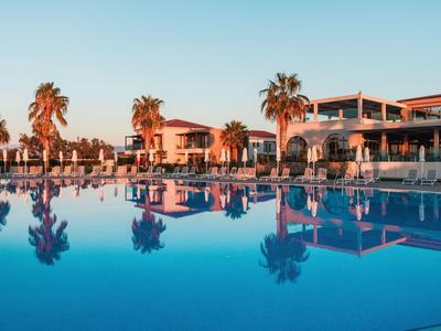 Luxury pool area with palm trees and modern hotel architecture at sunset.