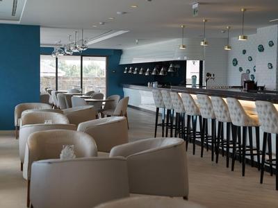 Modern hotel bar interior with light armchairs and a long bar stool area.
