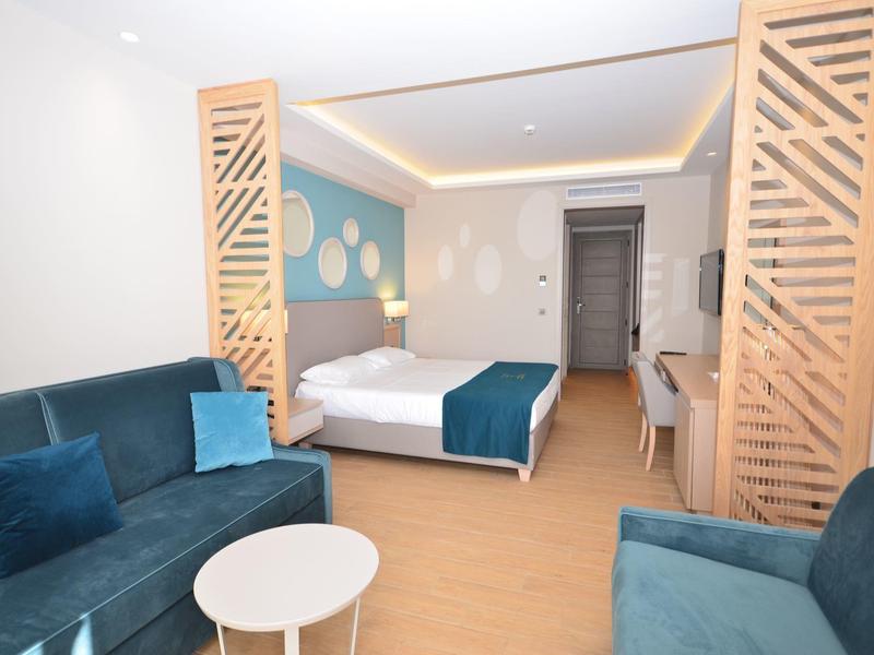 Modernes Hotelzimmer mit Sofa, Doppelbett, Holzgitterwänden und hellem Parkettboden.