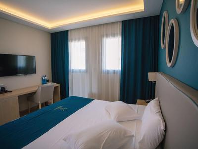 Modernes Schlafzimmer mit blauem Wandakzent, Doppelbett, Schreibtisch und Fernseher an der Wand.