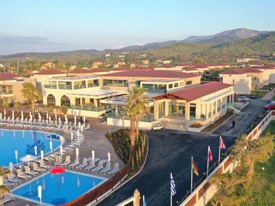 Große Hotelanlage mit blauem Pool, Sonnenschirmen, Palmen und Bergen im Hintergrund.