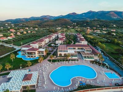 Große Hotelanlage mit mehreren Gebäuden, zwei geschwungenen blauen Swimmingpools und grüner Hügellandschaft.