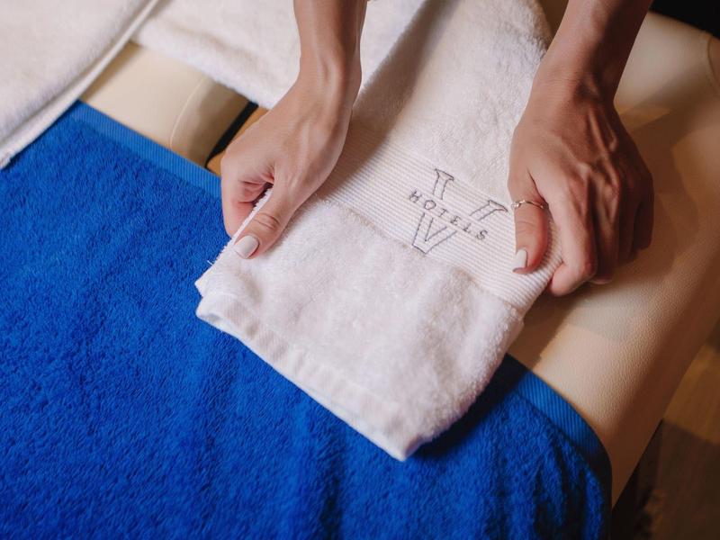 Zwei Hände falten ein weißes Handtuch auf einer blauen Decke auf einem gepolsterten Tisch.