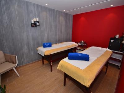 Zimmer mit zwei Massageliegen, roten und grauen Wänden, Holzboden und braunen Sesseln.