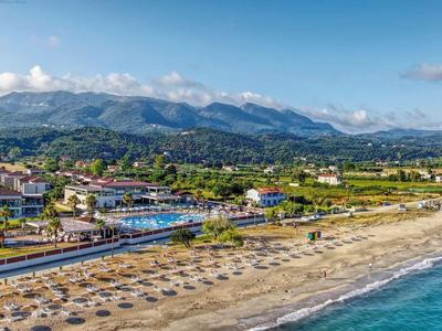 Plage avec parasols et vue sur un village côtier au pied des montagnes sous un ciel bleu.