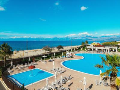 Espace piscine d'hôtel avec deux piscines, chaises longues et vue sur la mer par ciel clair.