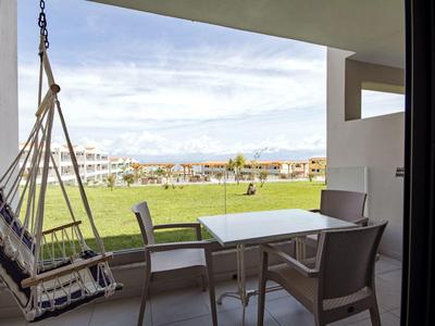 Balkon mit Hängesessel, Tisch und Stühlen, Blick auf eine grüne Wiese und Häuser im Hintergrund.