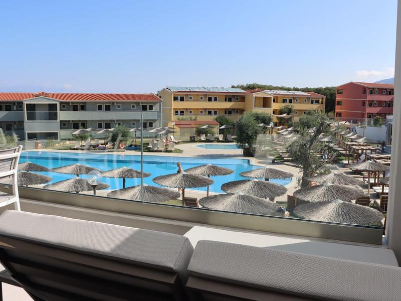 Blick auf einen Pool mit Sonnenschirmen, Palmen und angrenzenden mehrstöckigen Hotelgebäuden.