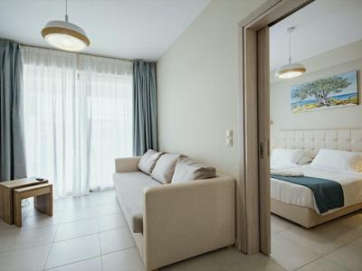 Modernes Zimmer mit Sofa, Tisch, großen Fenstern und angrenzendem Schlafzimmer mit Doppelbett.