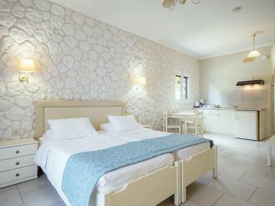 Helles Schlafzimmer mit Doppelbett, weißen Möbeln und minimalistischer Küchenzeile im Hintergrund.