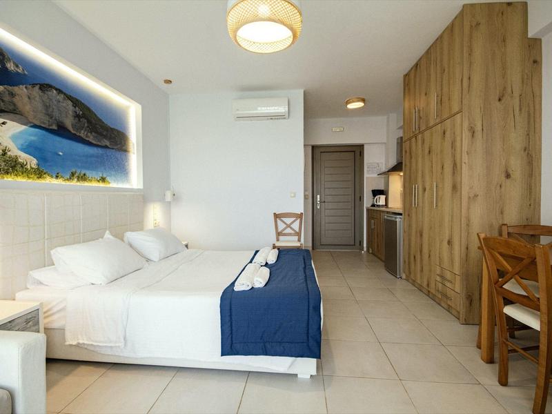 Modernes Hotelzimmer mit Doppelbett, blauer Decke, Holzmöbeln und großem Küstenbild an der Wand.